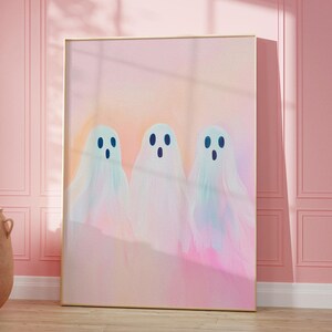 May include: A framed print of three pastel-colored ghosts with black eyes on a pink background.