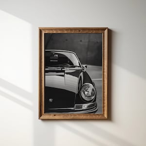 May include: Black and white photograph of a classic car, a Porsche 911, with the front headlight and hood visible.