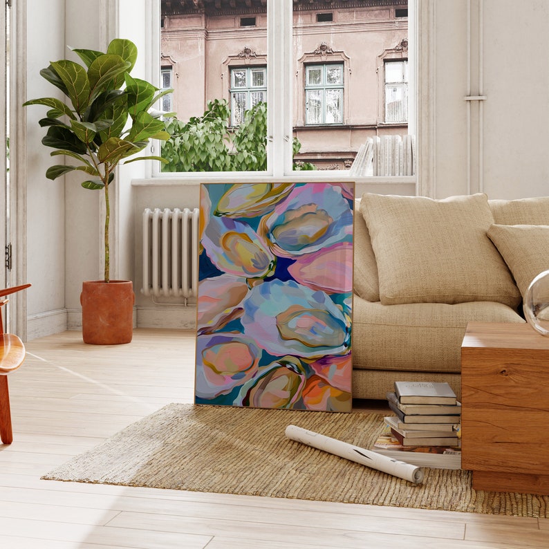 May include: Abstract painting of oyster shells in shades of pink, blue, and yellow. The painting is framed and hanging on a wall in a living room.