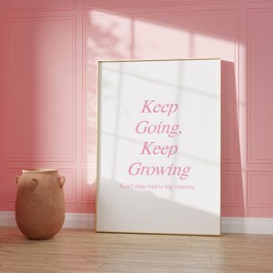Puede incluir: Un p&oacute;ster motivacional enmarcado con fondo rosa y texto blanco que dice "Keep Going, Keep Growing. Small steps lead to big victories."