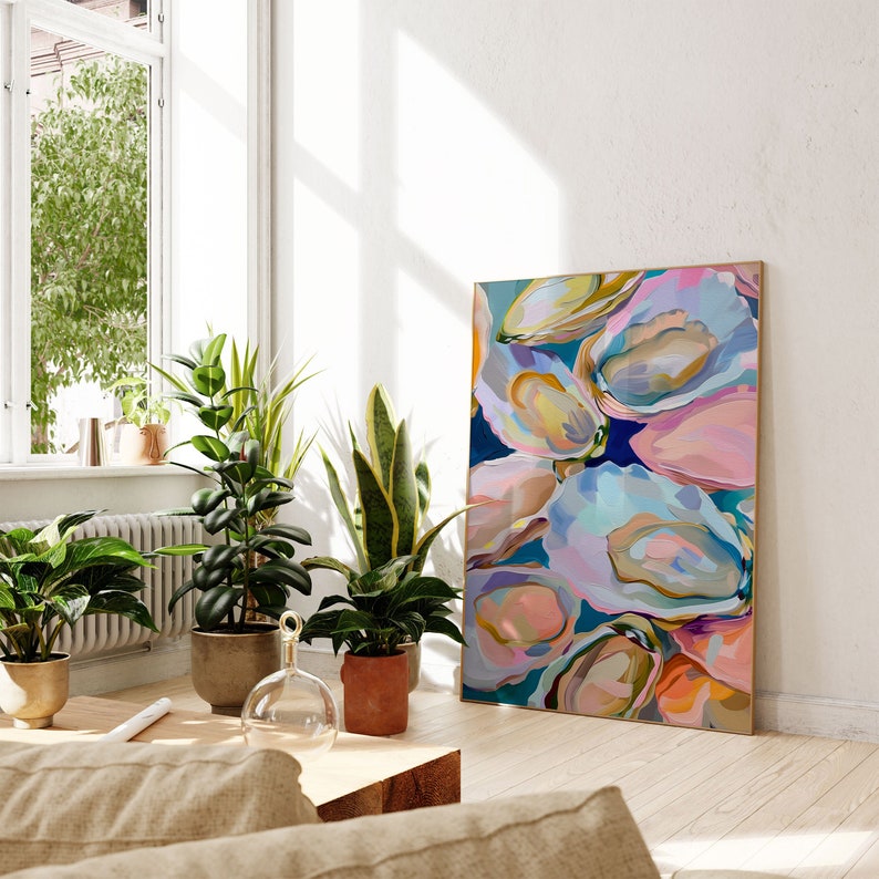 May include: Abstract painting of colorful oyster shells in shades of pink, blue, and yellow. The painting is framed and hanging on a white wall in a living room setting.