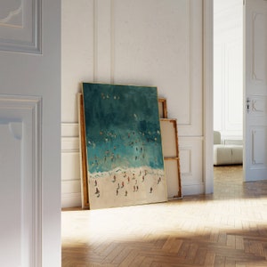 May include: A framed painting of a beach scene with a teal blue ocean and white sand. The painting depicts a large group of people swimming and sunbathing on the beach.