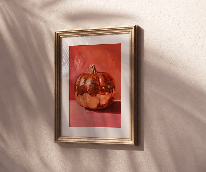 Pu&ograve; includere: Una stampa incorniciata di una zucca a forma di palla da discoteca dorata su sfondo rosa.