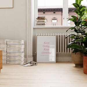 Puede incluir: Un p&oacute;ster enmarcado blanco con el texto "Keep Going, Keep Growing" en letras rosas. El p&oacute;ster est&aacute; colgado en una pared blanca en una habitaci&oacute;n con una ventana y un radiador.