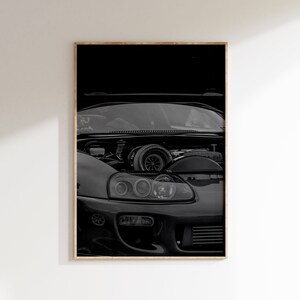 May include: A black and white wall art print featuring the front end of a sports car with its hood open. The engine bay reveals a prominent turbocharger, while the car's headlight assembly and front bumper intake are clearly visible in detail.