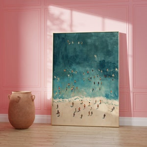 May include: A framed painting of an aerial view of a beach with people swimming and sunbathing in the turquoise water. The beach is white sand and the water is a light blue color.