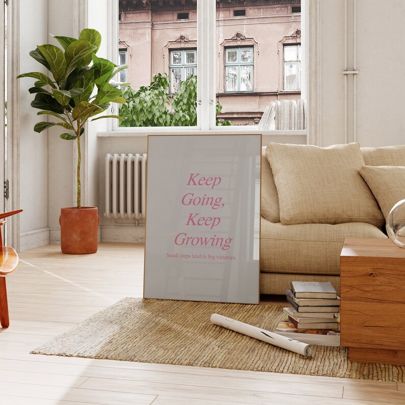 Puede incluir: Un p&oacute;ster motivacional con fondo gris claro y marco dorado. El texto "Keep Going, Keep Growing" est&aacute; escrito en cursiva rosa. El texto "Small steps lead to big victories" est&aacute; escrito en negro, m&aacute;s peque&ntilde;o, debajo del texto principal.