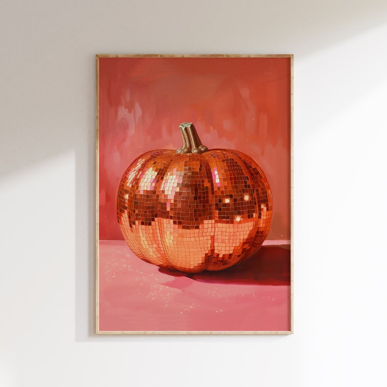 Pu&ograve; includere: Una grande zucca arancione ricoperta di piastrelle lucide a specchio. La zucca &egrave; appoggiata su una superficie rosa ed &egrave; incorniciata da una cornice in legno chiaro.