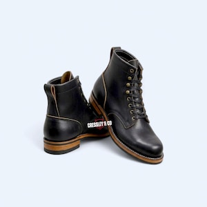 Könnte beinhalten: Schwarze Leder-Ankle Boots mit braunen Sohlen und Akzenten. Die Stiefel haben ein Schnürdesign mit Messingösen und einer Zuglasche. Der Markenname "CRESSLEY & CO" ist sichtbar. Stilvolle Schuhe.