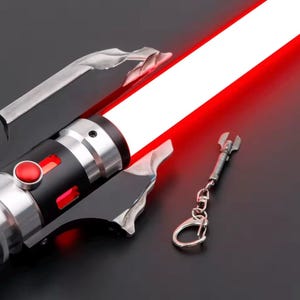 May include: A red and silver lightsaber with a bright red blade. The hilt is black and silver with a red button. A small silver wrench-shaped keyring hangs nearby. The lightsaber has a futuristic design.