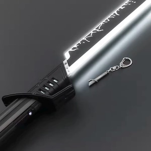 May include: A black and silver lightsaber with a bright white blade. The hilt has a sleek design with a few buttons. A small keychain replica of the lightsaber is also included, with a silver finish. The lightsaber is a prop or collectible.