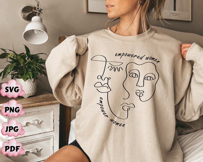 May include: A beige sweatshirt with a black line drawing of three faces and the text "empowered women" repeated twice.