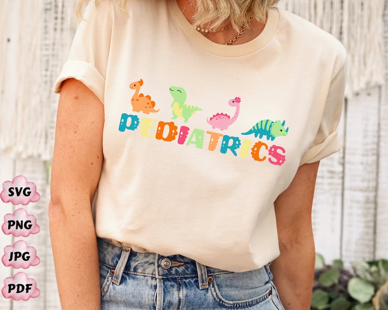 May include: A white t-shirt with the word "PEDIATRICS" spelled out in colorful letters. Each letter has a small cartoon dinosaur on it. The dinosaurs are green, orange, pink, and blue.
