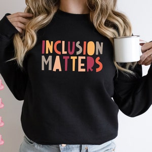 May include: A black sweatshirt with the text "INCLUSION MATTERS" in colorful block letters. The letters are in shades of orange, red, yellow, and brown.