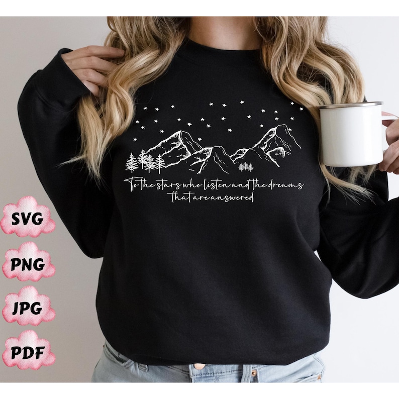 Op de afbeelding: Zwart sweatshirt met een wit grafisch ontwerp van bergen, sterren en bomen. De tekst "To the stars who listen and the dreams that are answered" staat op het sweatshirt gedrukt.