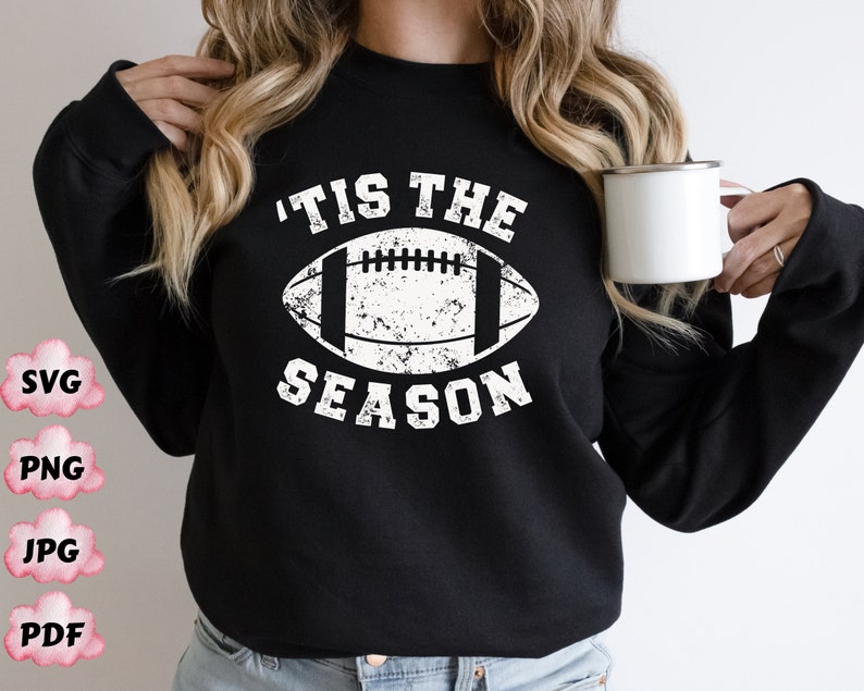 May include: Black sweatshirt with a white distressed graphic of a football and the text 'Tis the Season'.