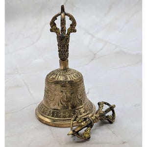 May include: A detailed shot of a brass bell and a dorje, a ritual object. The bell has an ornate handle and detailed carvings. The dorje is lying next to the bell. Both objects have a golden hue.