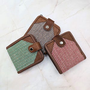May include: Three wallets with brown leather accents and herringbone fabric in green, black and white, and red and white. Each wallet has a snap closure and a brown leather flap.