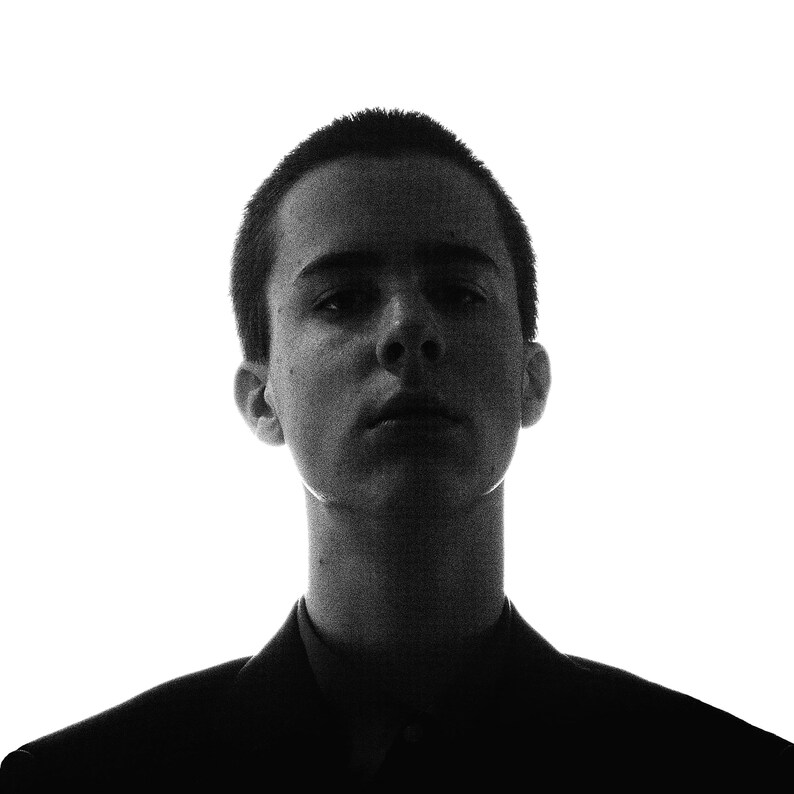 May include: A black and white portrait of a person with short hair. The person is looking directly at the camera with a serious expression.