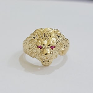 May include: A gold lion head ring with red gemstone eyes.