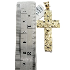 May include: A gold-tone Jesus on the cross pendant with a textured design. The pendant is 2 inches tall and is measured against a ruler.