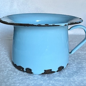 Op de afbeelding: Een lichtblauwe emaille kan met een handvat en een versleten, roestige rand. De kan heeft een brede, ondiepe opening en een rond lichaam.