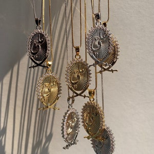 May include: A group of seven silver and gold necklaces with pendants featuring a stylized Arabic inscription surrounded by a circle of clear rhinestones. Each pendant is attached to a delicate chain.
