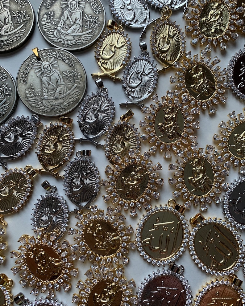May include: A collection of gold and silver pendants with intricate designs and clear crystals. The pendants feature Arabic calligraphy and religious symbols.