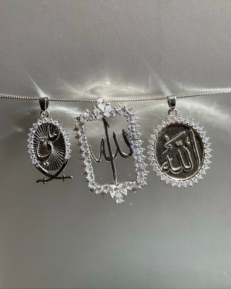 May include: Three silver pendants with clear crystal accents. The pendants feature the Arabic word "Allah" in different styles.