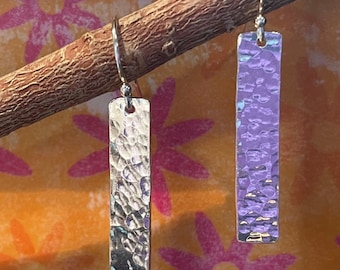 May include: A pair of silver earrings with a hammered texture. The earrings are rectangular in shape and hang from a silver hook.