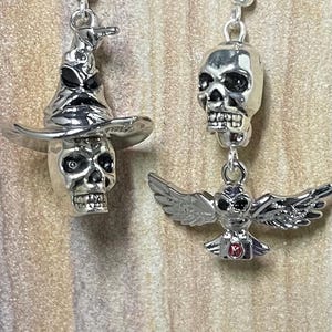May include: A pair of silver earrings with a skull and a wizard's hat on one earring and a skull and an owl on the other earring.
