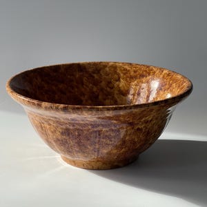 May include: A brown and yellow glazed ceramic bowl with a wavy rim. The bowl has a mottled, speckled appearance.