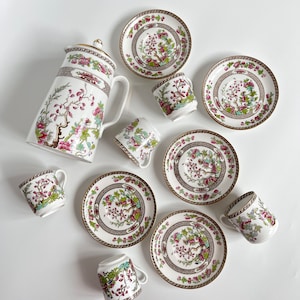 May include: A white tea set with a floral pattern in shades of pink, green, and gold. The set includes a teapot, six cups, and six saucers.