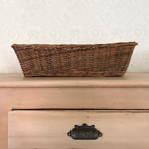 Peut inclure: Un panier rectangulaire en osier tressé avec une finition marron naturel. Le panier présente un motif de tissage serré et entrelacé sur toute sa structure, créant un contenant robuste et fonctionnel avec une base plate et des côtés évasés.