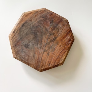 May include: A hexagonal wooden board with a natural brown finish, featuring visible wood grain patterns, knots, and a textured surface. The edges are straight and angled, creating a geometric shape with a flat top surface and a sturdy construction.