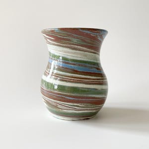 May include: A ceramic vase with a wide, rounded body and a flared rim. The vase features a swirled pattern of brown, green, white, and blue horizontal stripes. The vase is approximately 8 inches tall.