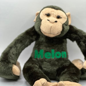 May include: A plush green monkey toy with a tan face and brown eyes. The monkey is sitting with its legs crossed and has the name "Melon" embroidered on its chest in green.