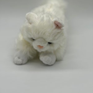 May include: A plush white cat toy with soft, fluffy fur. The cat has a pink nose and ears, and its paws are visible. The toy is positioned on a white background, giving it a clean and simple appearance.