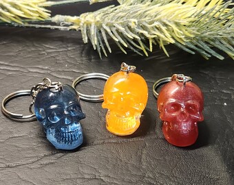 May include: Three resin skull keychains in blue, orange, and red. Each skull has a silver key ring attached.