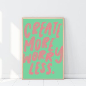May include: A framed poster with a green background and pink text that reads "CREATE MORE WORRY LESS."