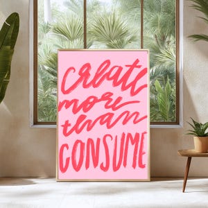 Peut inclure: Impression d'art encadrée rose avec le texte "create more than consume" en lettres rouges audacieuses.
