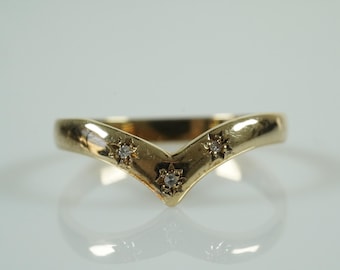 Op de afbeelding: Een goudkleurige chevronring met drie kleine, stervormige diamantaccenten. De ring heeft een gladde, gepolijste afwerking en is geplaatst tegen een witte achtergrond. Het ontwerp van de ring is een V-vorm.