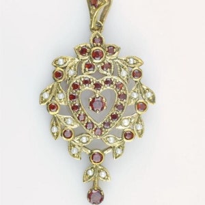 Puede incluir: Un colgante de oro con un diseño en forma de corazón engastado con granates rojos y perlas blancas.