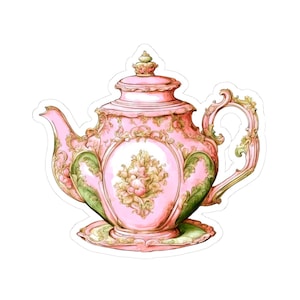 May include: A pink and green decorative teapot with ornate floral designs. The teapot features a detailed handle, spout, and lid, and sits on a matching saucer. The design includes gold accents and a central floral motif.