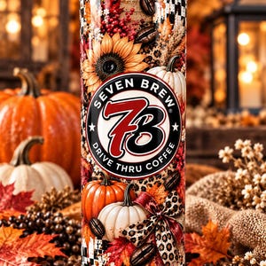 May include: A cylindrical tumbler with a clear lid and straw, featuring a fall-themed design with sunflowers, pumpkins, coffee beans, and a leopard print bow. The center displays a circular logo with the text Seven Brew 73 Drive Thru Coffee.