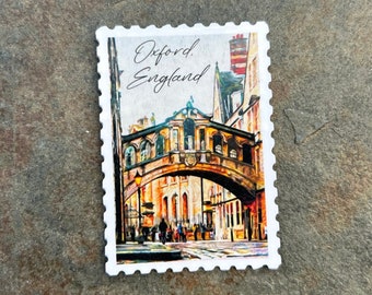 May include: A white postage stamp featuring a watercolor painting of the Bridge of Sighs in Oxford, England. The stamp has the words "Oxford. England" in script. The bridge is arched and has several windows.