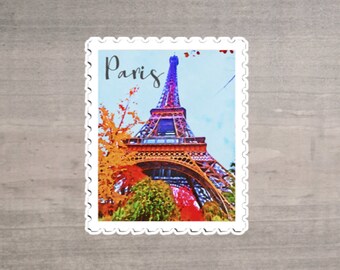 May include: A postage stamp-shaped sticker featuring a watercolor painting of the Eiffel Tower in Paris. The tower is depicted in shades of red, orange, and blue, with the word "Paris" written in script above it. The sticker has a white border.