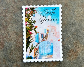 May include: A white stamp with a colorful image of a building in Crete, Greece. The building has blue doors and shutters, with pink flowers and green leaves. The text "Crete, Greece" is written in cursive.