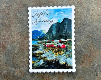 May include: A white, postage stamp-shaped sticker featuring a scenic view of Lofoten, Norway. The image depicts red buildings on the coast, mountains, and the text "Lofoten Norway" in a script font. The sticker has a serrated edge.