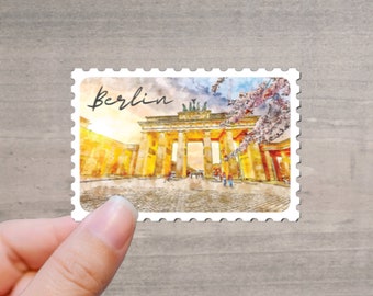 May include: A watercolor-style stamp featuring the Brandenburg Gate in Berlin, Germany, with the word "Berlin" in script. The image has a warm color palette with hints of pink blossoms.